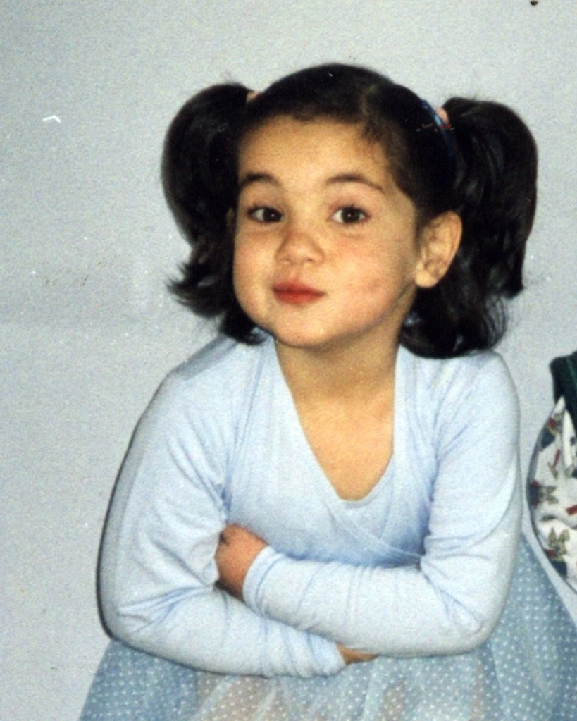a toddler in pigtails wearing a ballet uniform